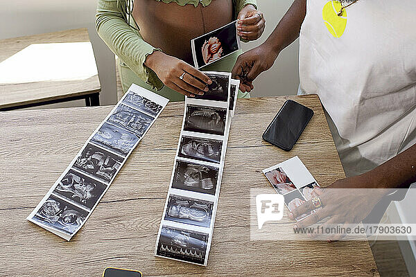 Pregnant woman by man with ultrasound photos of baby on table