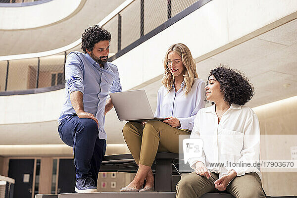 Happy businesswoman discussing with colleagues over laptop in corridor