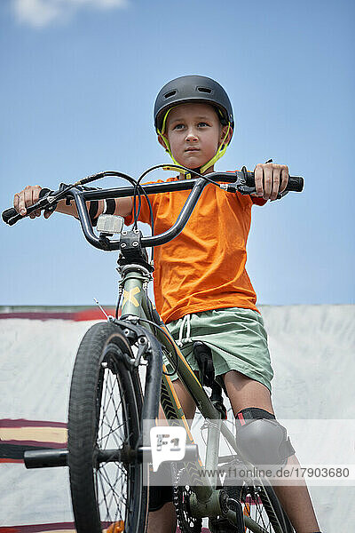 Determined boy sitting on BMX bike at skateboard park