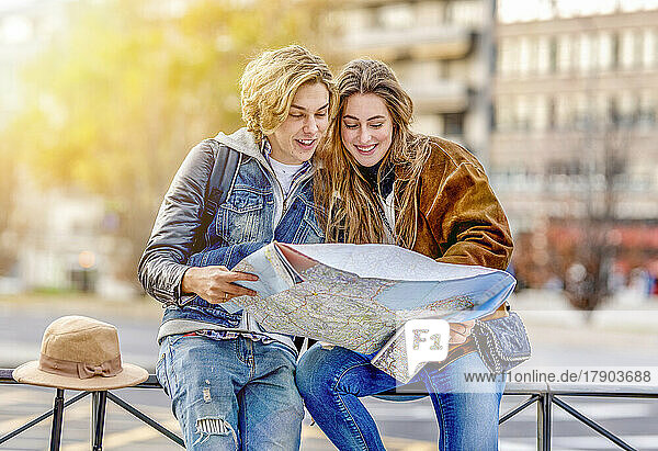 Lächelnder Mann und Frau  die auf dem Geländer sitzen und auf die Karte schauen