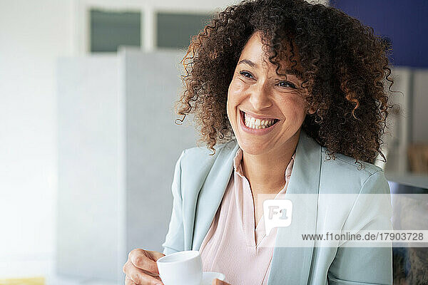 Glückliche Geschäftsfrau  die in der Pause im Büro eine Tasse Kaffee trinkt