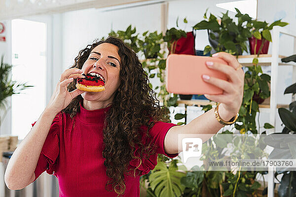 Junge Geschäftsfrau isst Donut und macht in der Cafeteria ein Selfie mit dem Handy