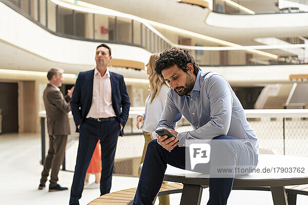 Businessman using mobile phone with colleagues in background at office