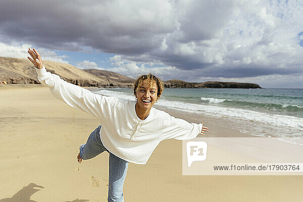 Glückliche Frau mit ausgestreckten Armen  die an einem sonnigen Tag am Strand genießt