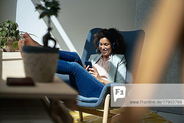 Happy businesswoman using mobile phone sitting on chair at workplace