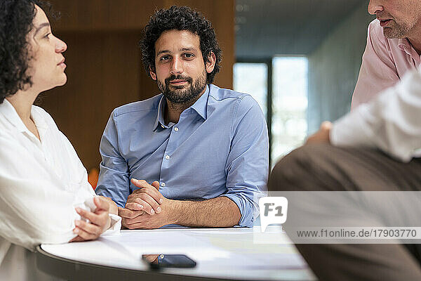 Confident businessman by colleagues discussing in meeting at office