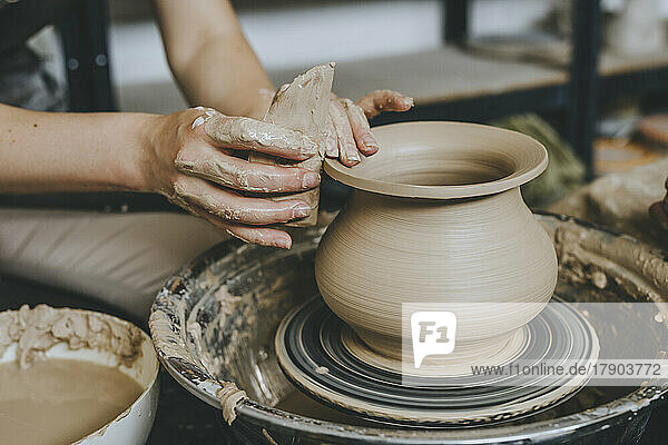 Hands of potter molding pot on pottery wheel at workshop