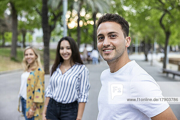 Smiling young man standing in front of friends at park