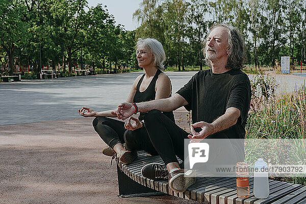 Paar sitzt auf Bank und meditiert im Park
