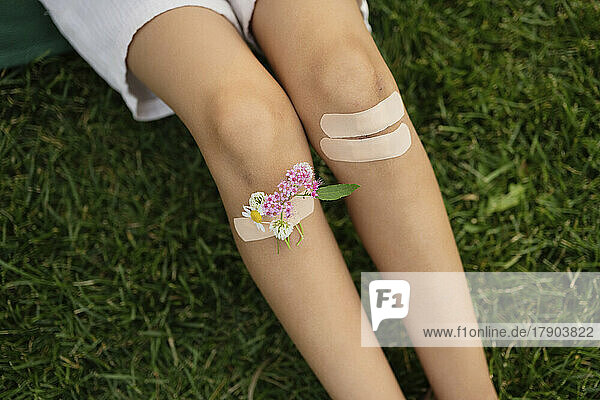 Mädchen mit bandagierten Knien und Blumen sitzt im Gras