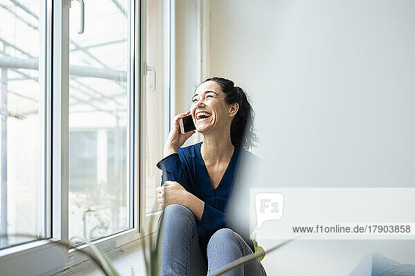 Happy woman talking on mobile phone sitting by window