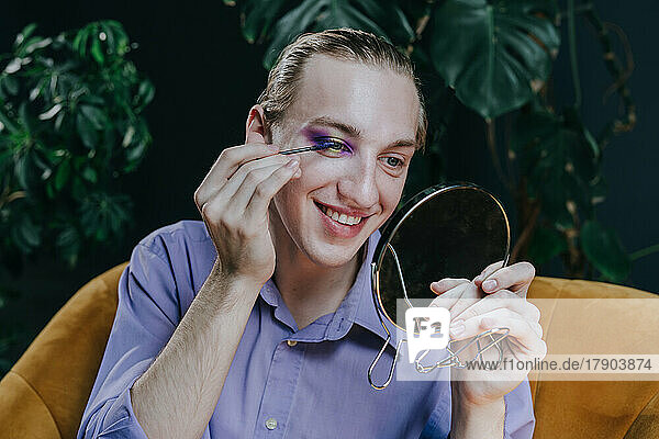 Lächelnder Make-up-Künstler  der Mascara aufträgt und in den Spiegel schaut