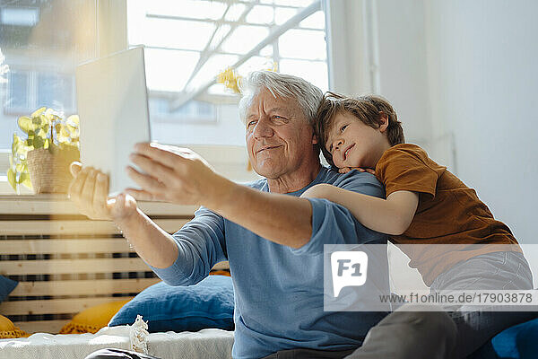 Senior man taking selfie with boy through tablet PC at home