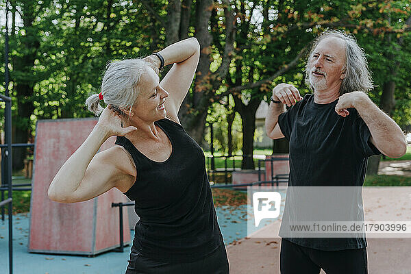Smiling mature woman with senior man doing warm up exercise in park