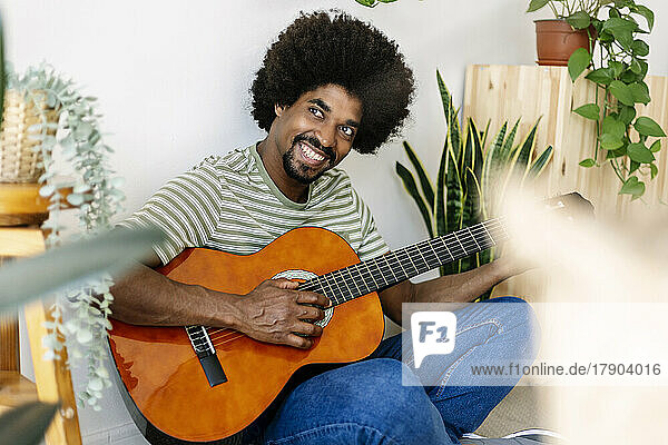 Happy man with Afro hairstyle practicing guitar at home