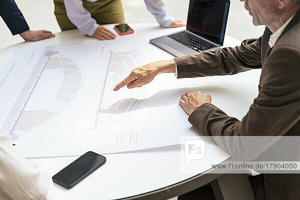 Businessman pointing at diagram on table in meeting with colleagues