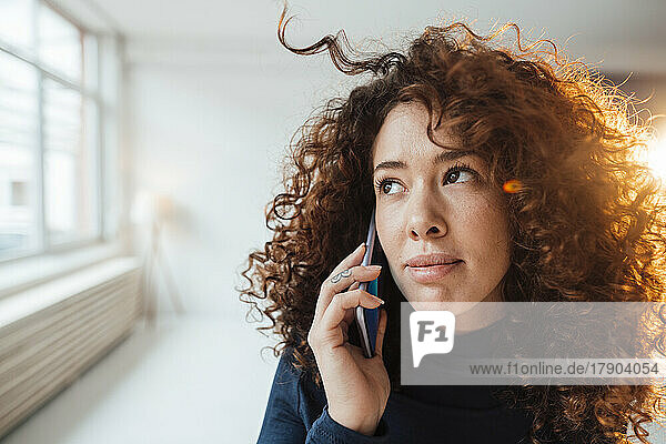 Beautiful woman with curly hair talking on smart phone contemplating