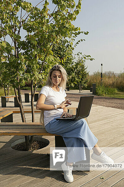 Freiberufler sitzt mit Laptop und überprüft die Zeit im Park