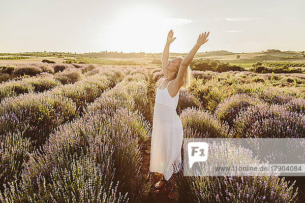 Frau steht mit erhobenen Armen inmitten von Lavendelblüten im Feld