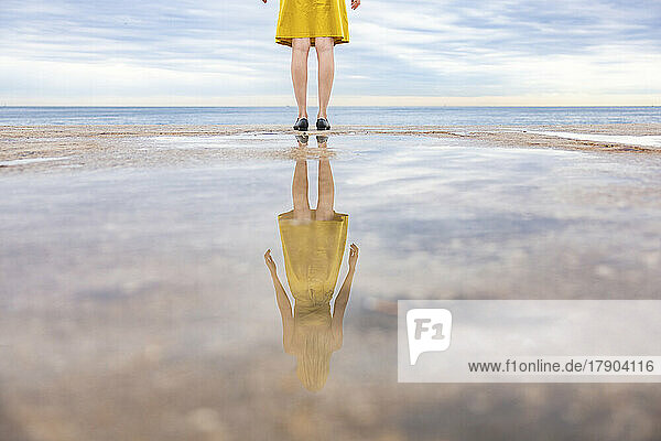 Reflection of woman in puddle standing at promenade