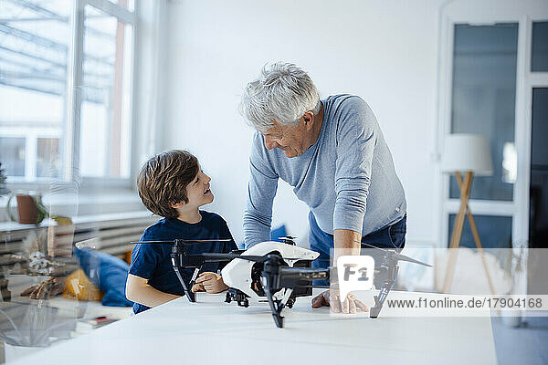 Grandfather and grandson talking with drone on table in living room