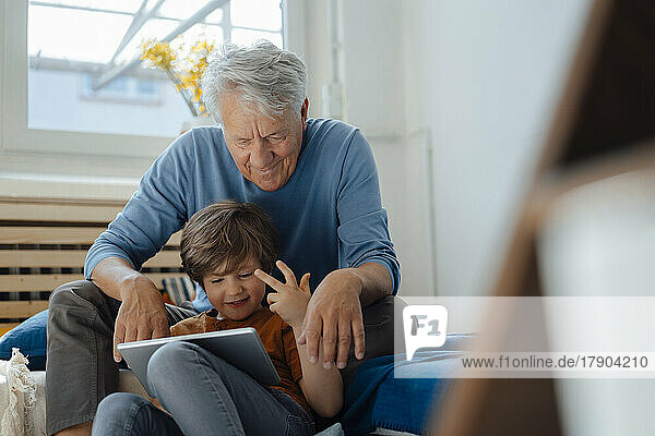 Happy boy sharing tablet PC with grandfather at home