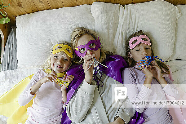 Mutter und Töchter mit Partyhornbläser liegen zu Hause im Bett