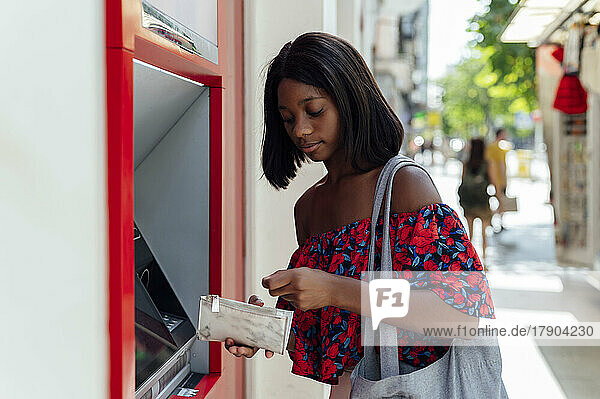 Junge Frau mit Handtasche steht am Geldautomaten