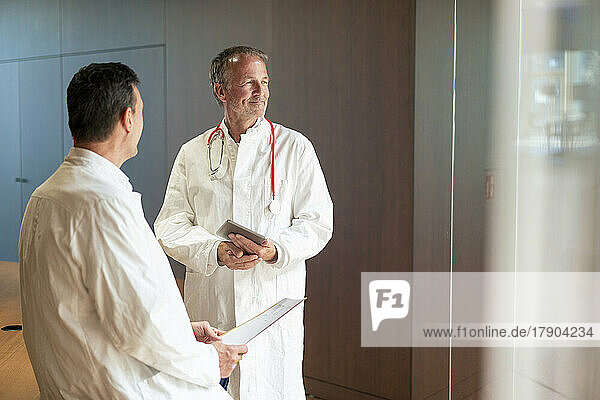 Smiling doctor holding tablet PC standing by colleague at hospital