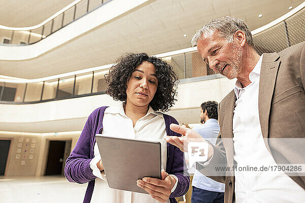Multiracial business colleagues discussing over tablet computer in corridor