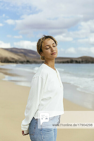 Entspannte Frau mit geschlossenen Augen steht am Strand