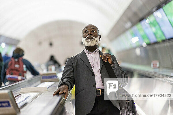 Contemplative businessman moving down on escalator at subway station