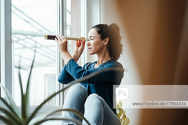 Curious woman looking through antique monocular sitting by window