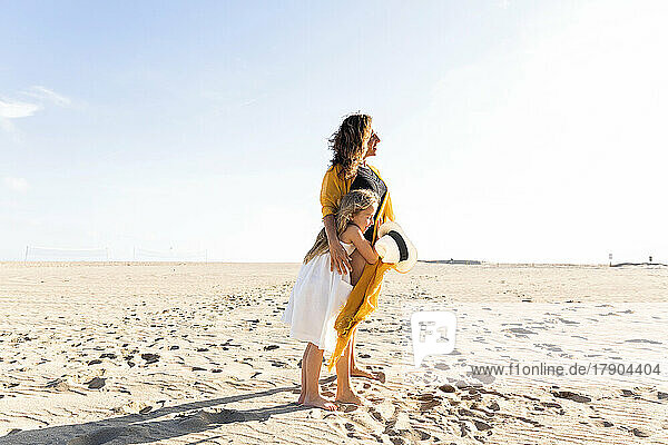Mädchen umarmt Mutter am Strand an einem sonnigen Tag