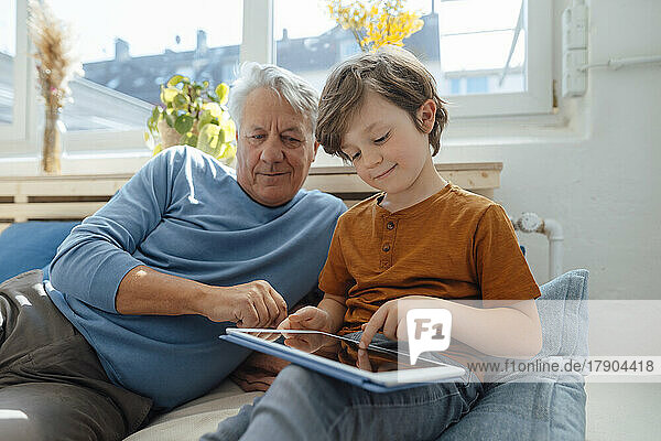 Boy using tablet PC by grandfather in living room