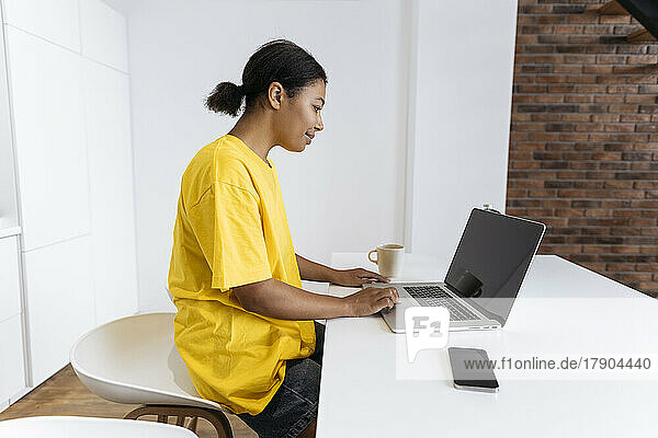 Junge Frau sitzt in der Küche und arbeitet am Laptop