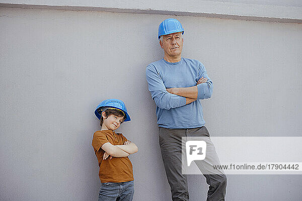 Grandson and grandfather with arms crossed in front of wall