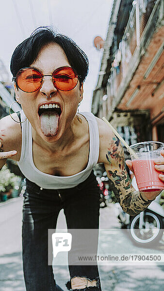 Tattooed woman sticking out tongue holding glass of drink