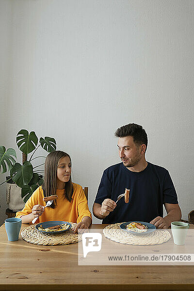 Smiling girl with father having breakfast on dining table