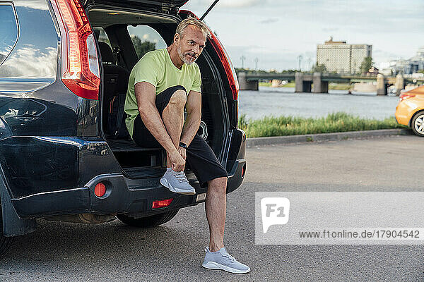 Reifer Mann sitzt im Kofferraum eines Autos und bindet Schnürsenkel