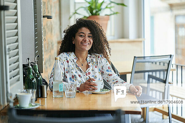 Glückliche junge Frau mit Kaffeetasse sitzt im Café