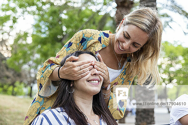 Happy woman covering eyes of friend at park
