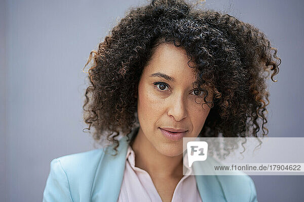 Confident businesswoman with curly hair in front of gray wall