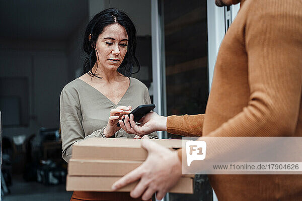 Woman receiving parcel and signing on smart phone at doorway