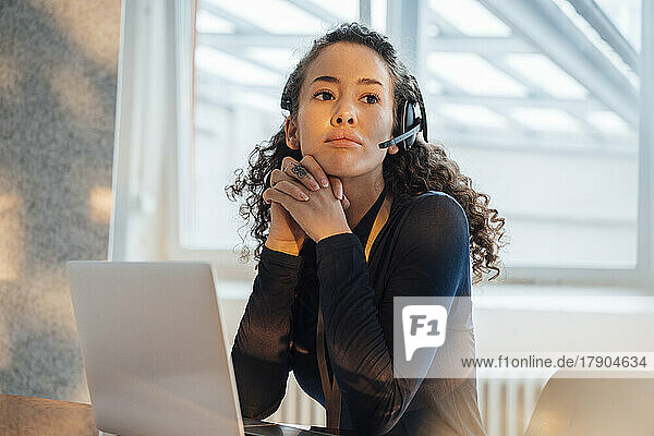 Young customer service representative sitting with hands clasped at desk in office