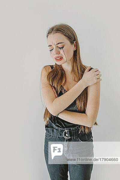 Depressed woman with hand on shoulder crying in front of wall