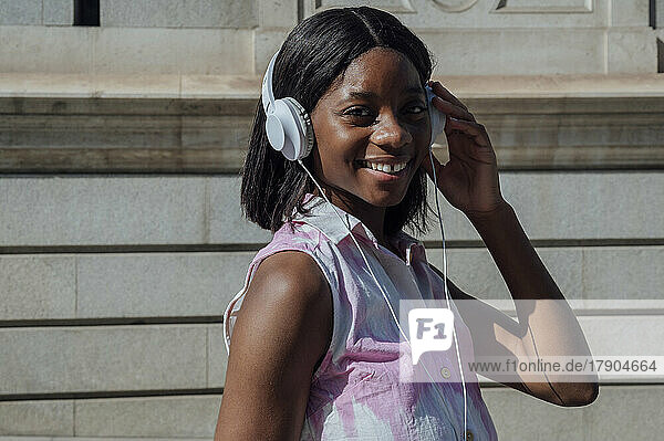 Happy woman listening music through headphones on sunny day