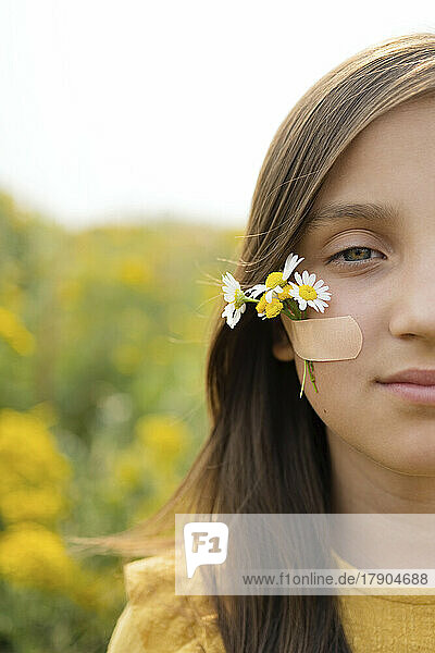 Girl with flowers attached on cheek by adhesive bandage