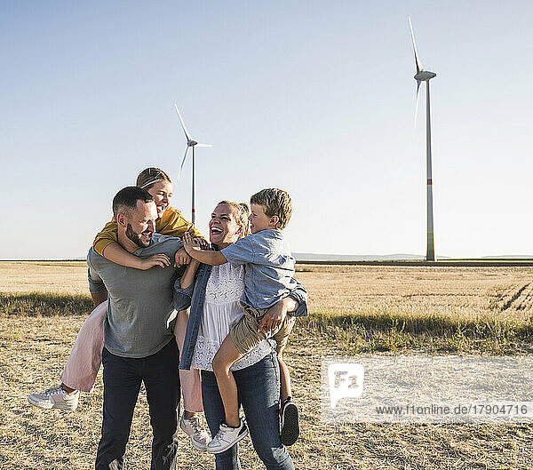 Confident family standing in wind park carrying kids