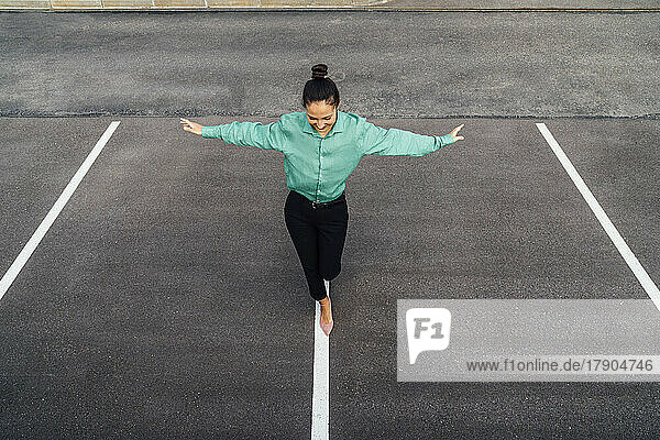 Smiling businesswoman with arms outstretched balancing on road marking